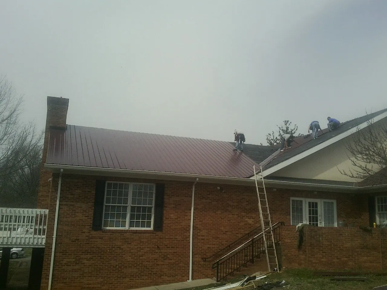 Crew setting red metal roofing panels on a brick home in Ashton